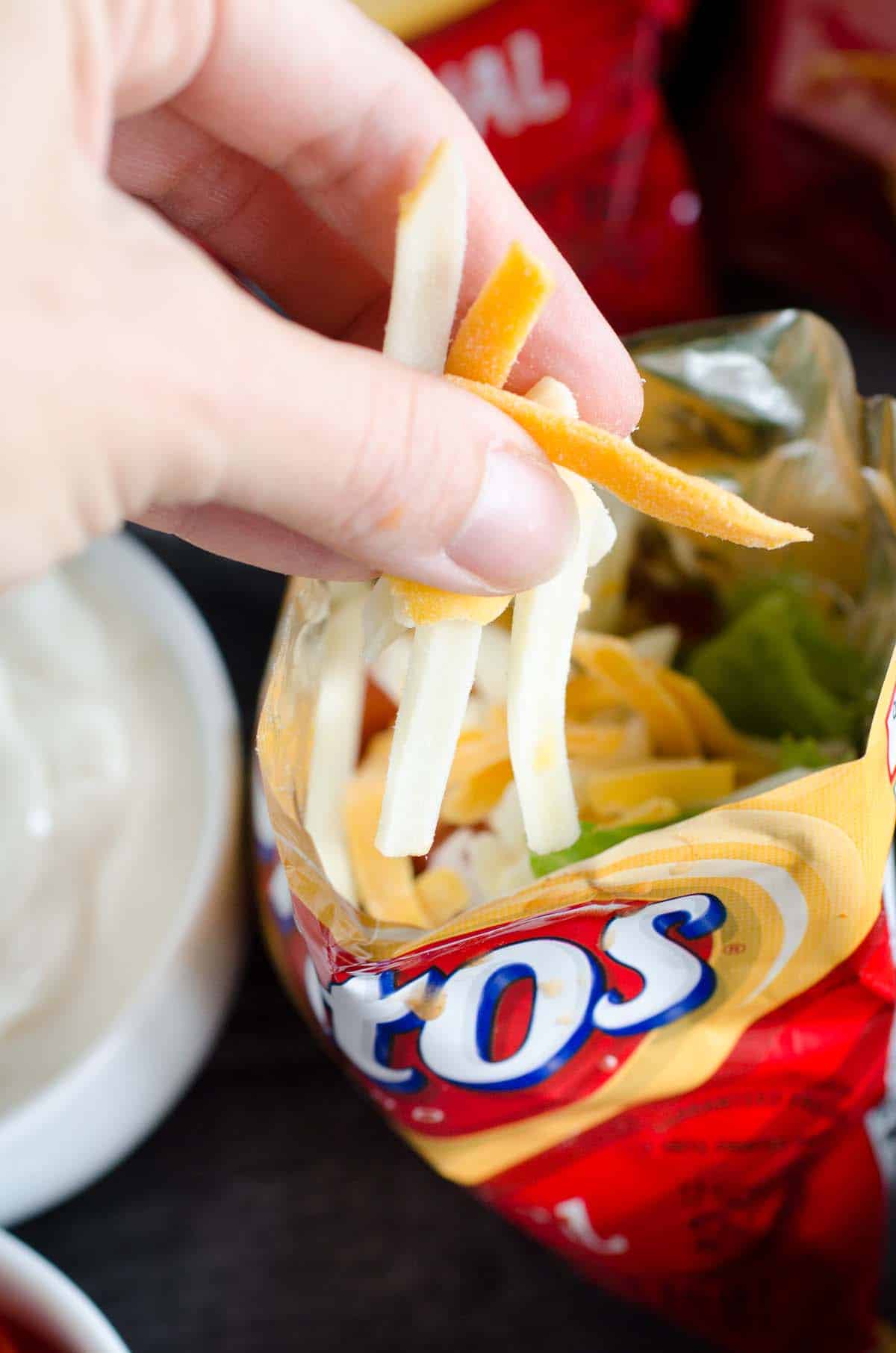 putting shredded cheese into bag of fritos
