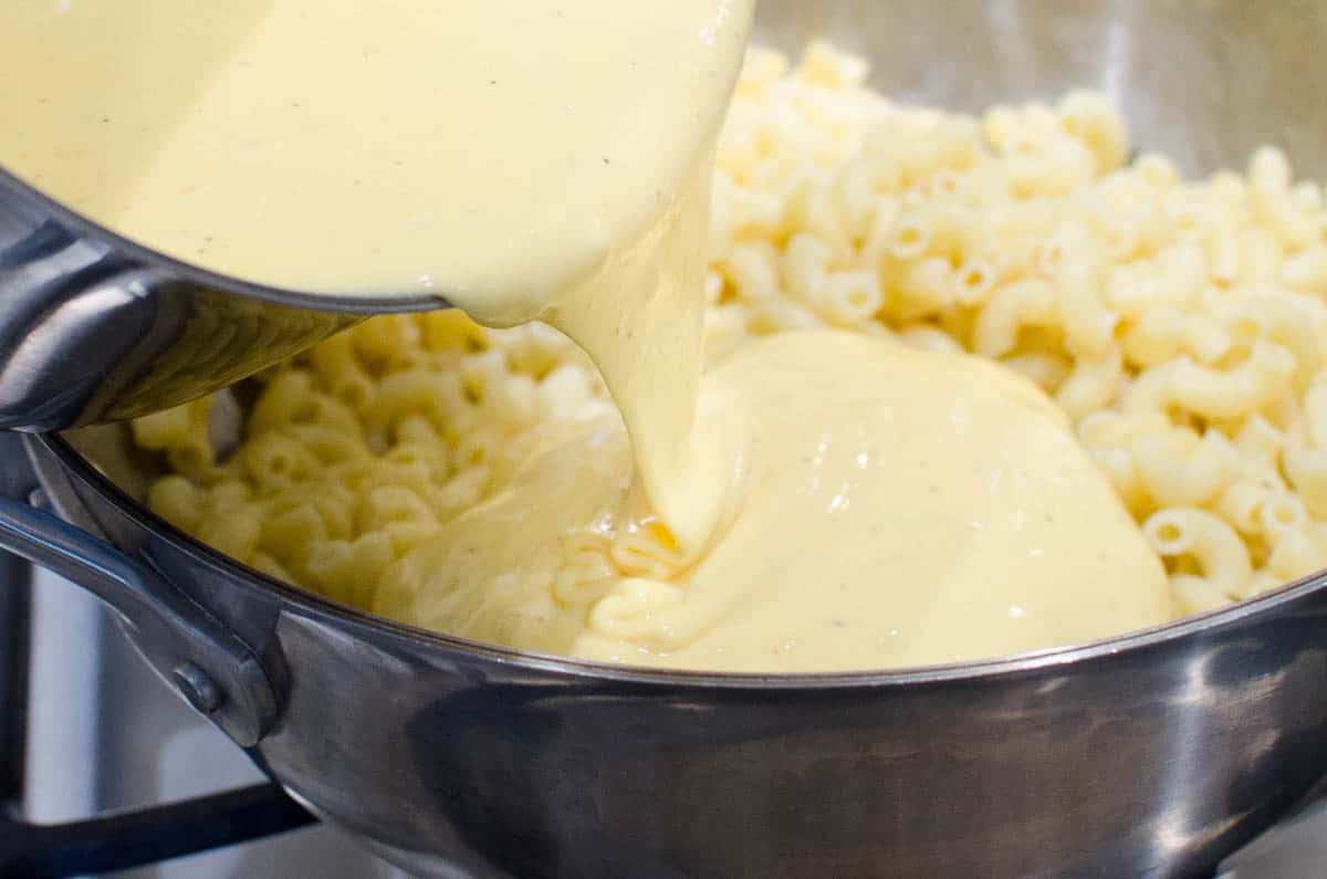 pouring cheese sauce into pot of macaroni