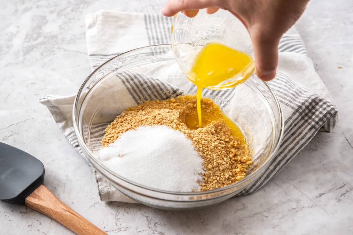 pouring butter into bowl with graham cracker crumbs and sugar