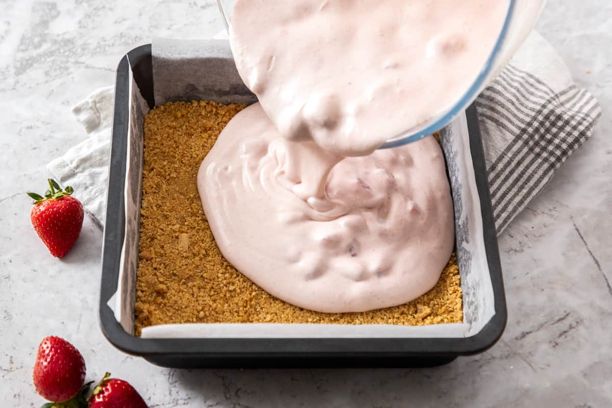 Pouring strawberry dessert mixture into square pan over graham cracker crust