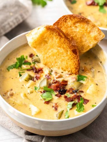 bowl of cheeseburger soup with toasted hamburger buns and topped with bacon