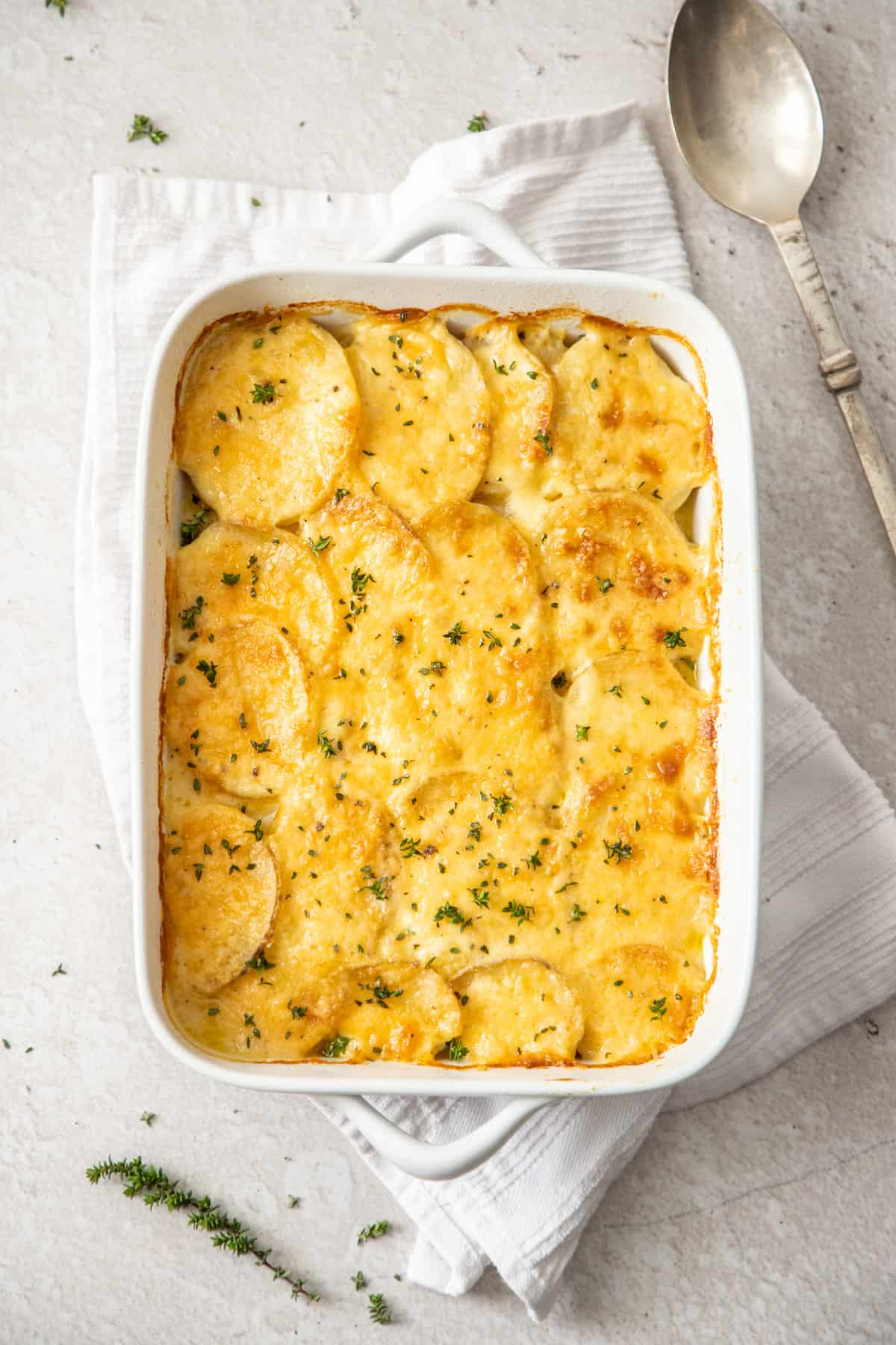 scalloped potatoes in white casserole dish with spoon on side