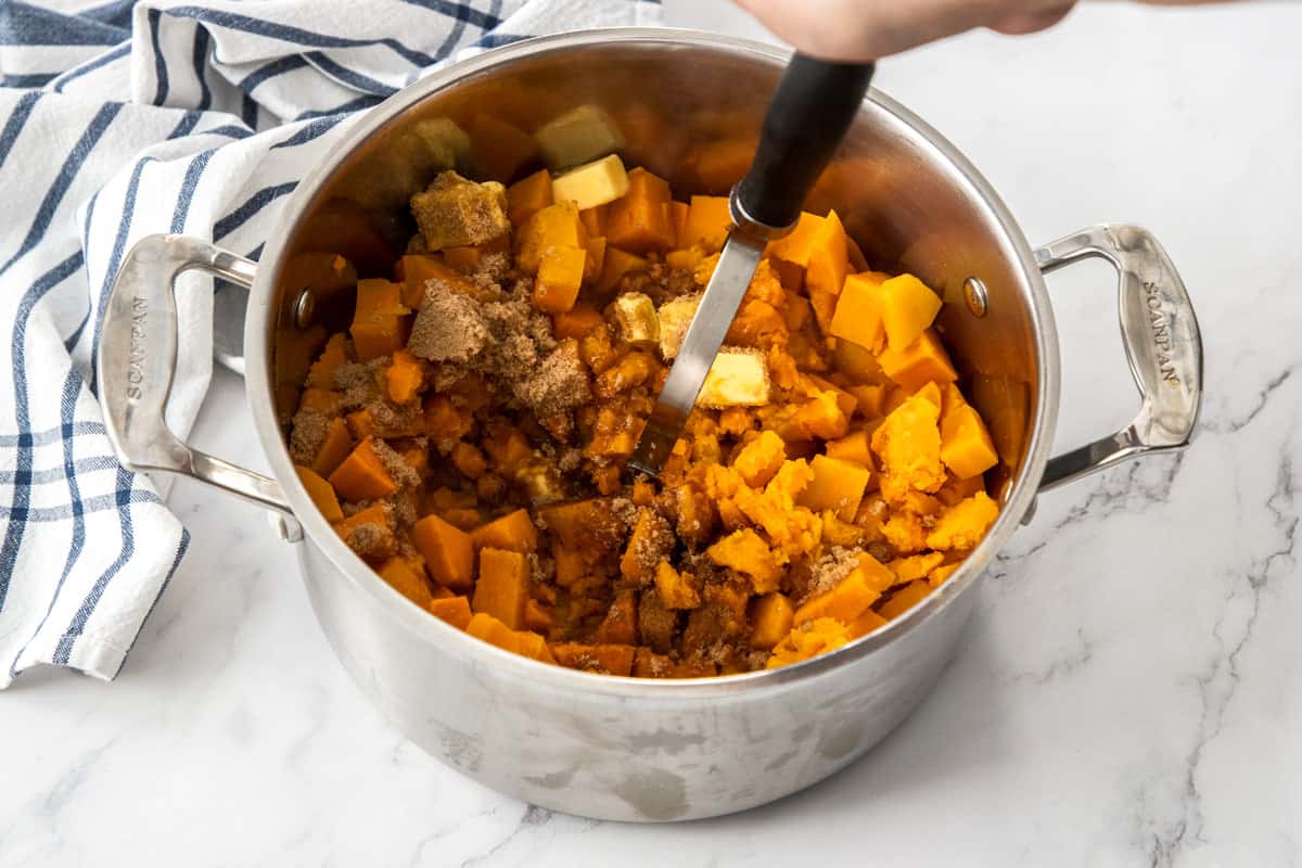 mashing sweet potatoes with brown sugar and butter in pot