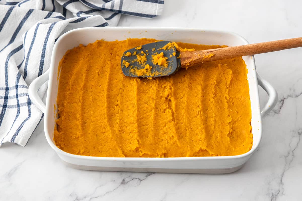 cooked sweet potatoes spread into casserole dish with spatula