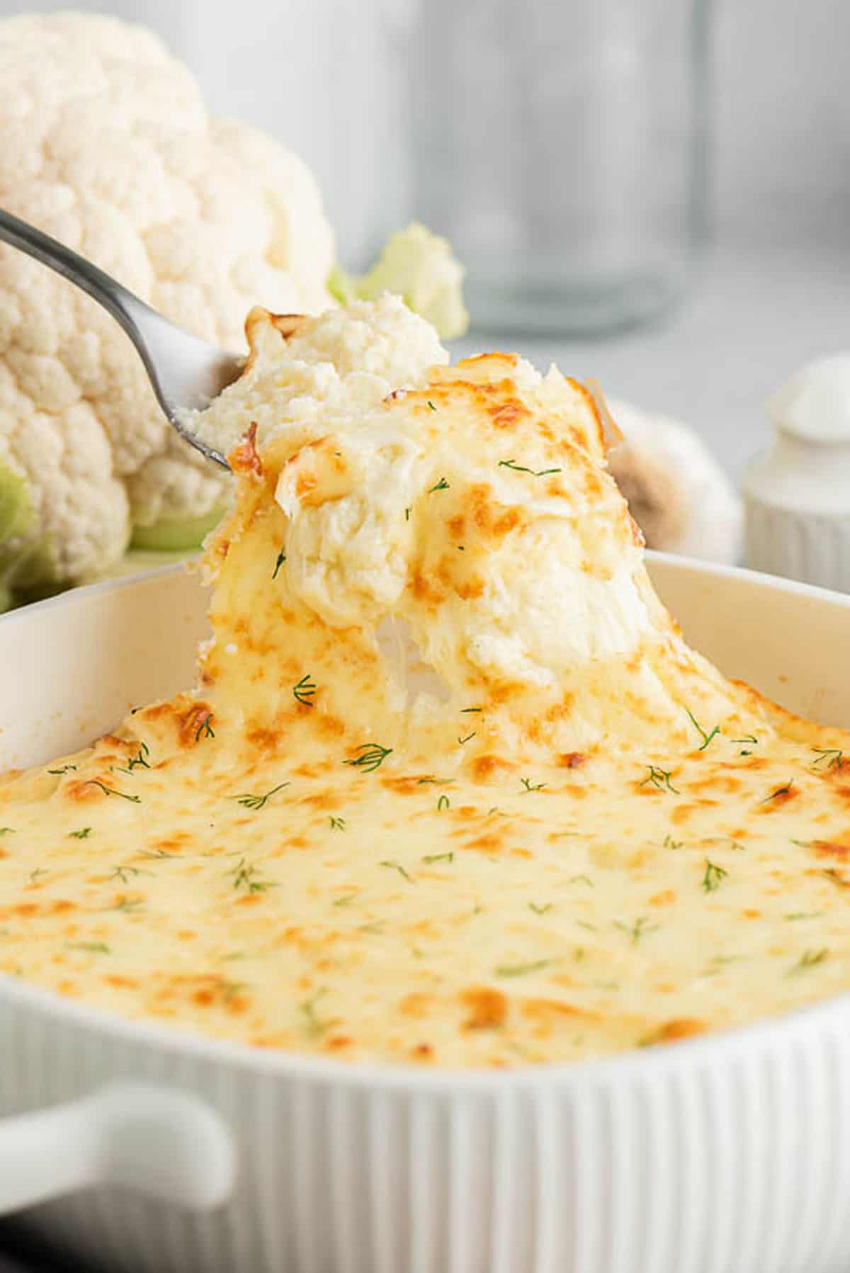 spooning cheesy mashed cauliflower out of casserole dish
