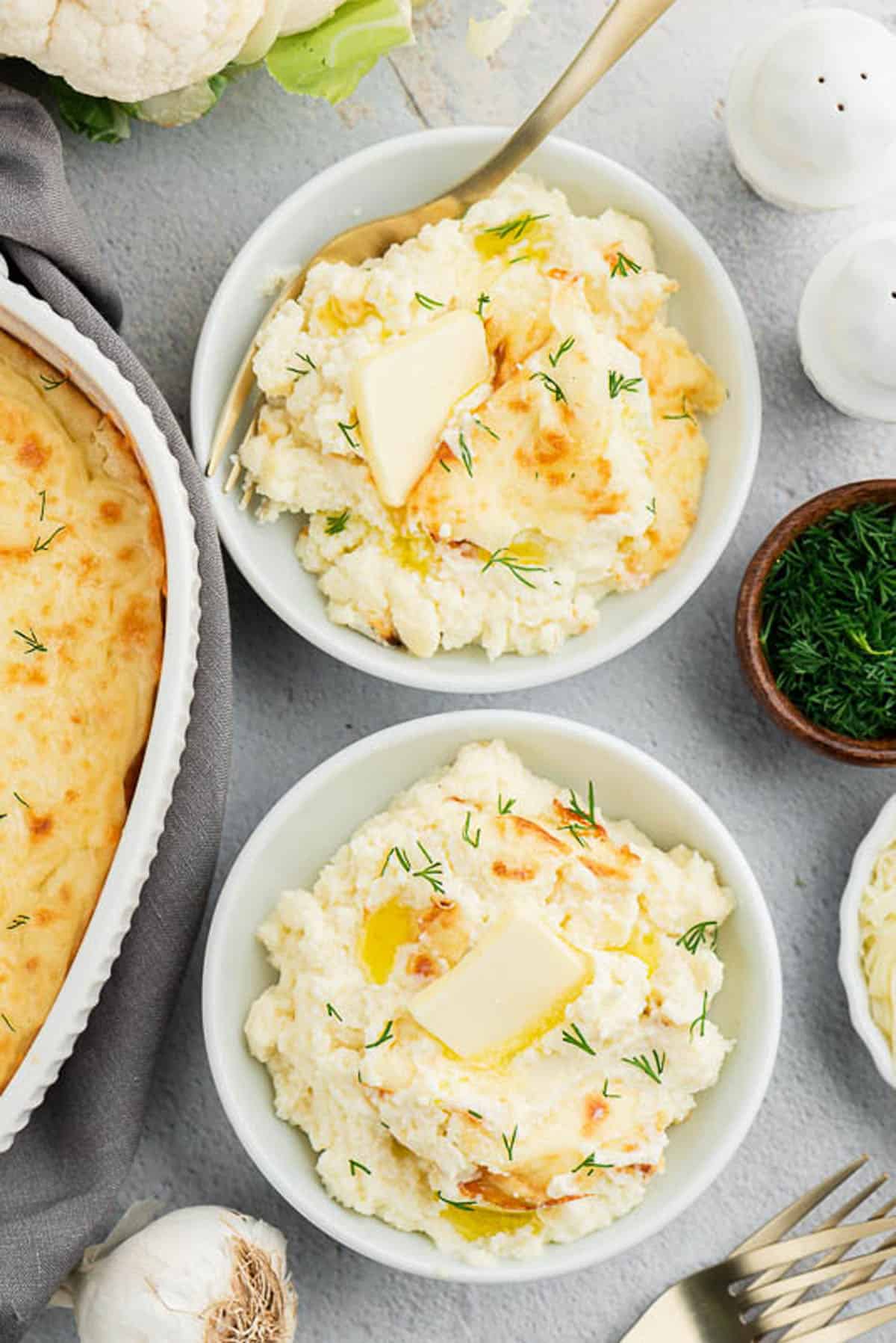 two bowls of mashed cauliflower topped with a butter square