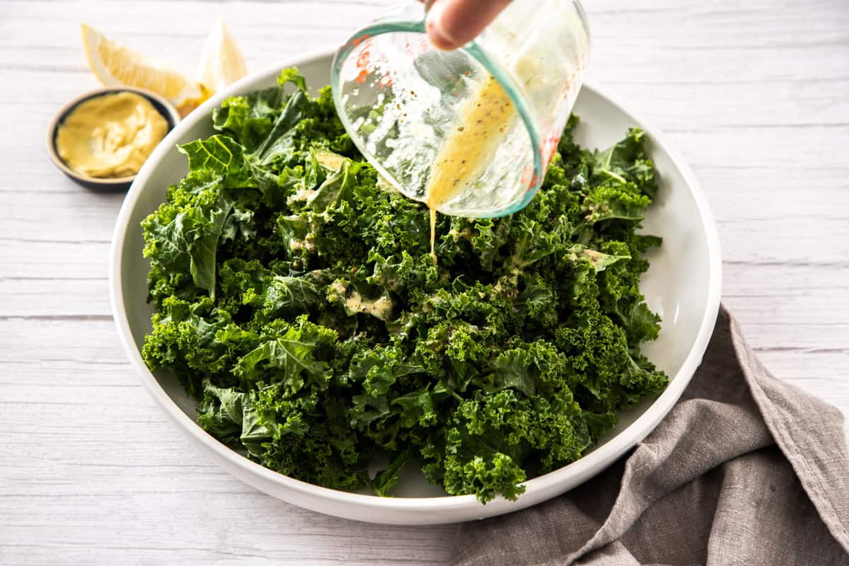 pouring dressing onto fresh kale in bowl