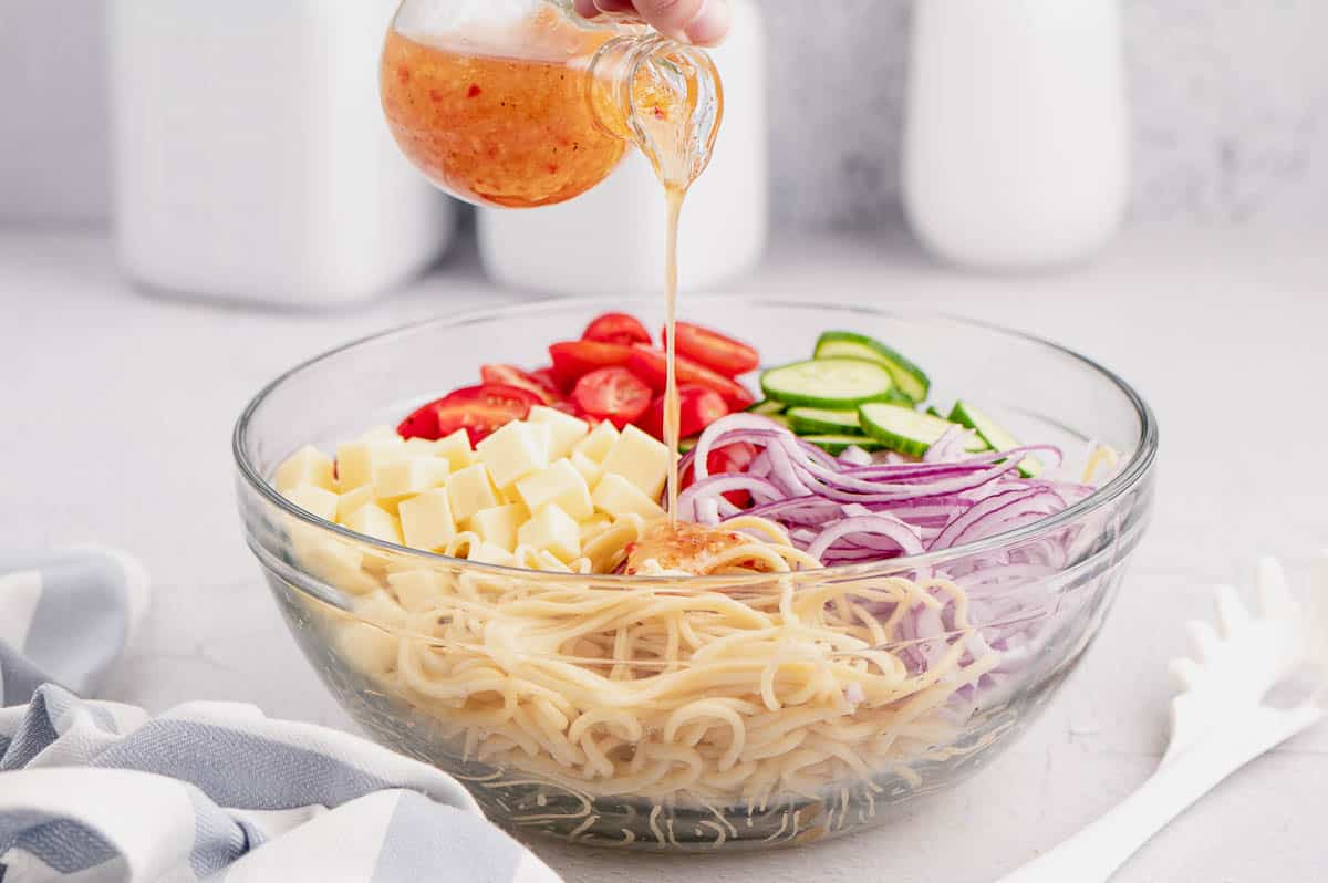 pouring dressing into clear bowl of spaghetti noodles and vegetables