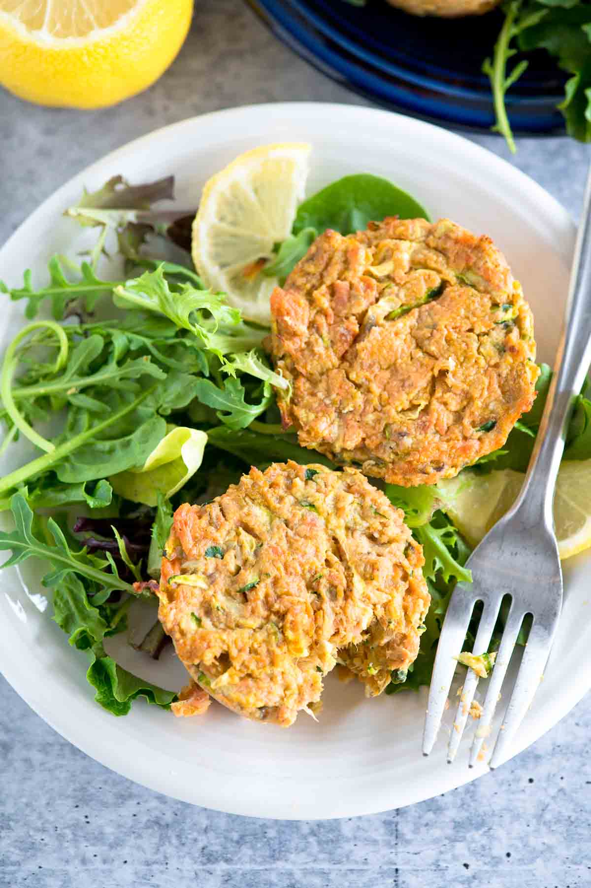 two salmon patties on a plate with salad greens and a fork