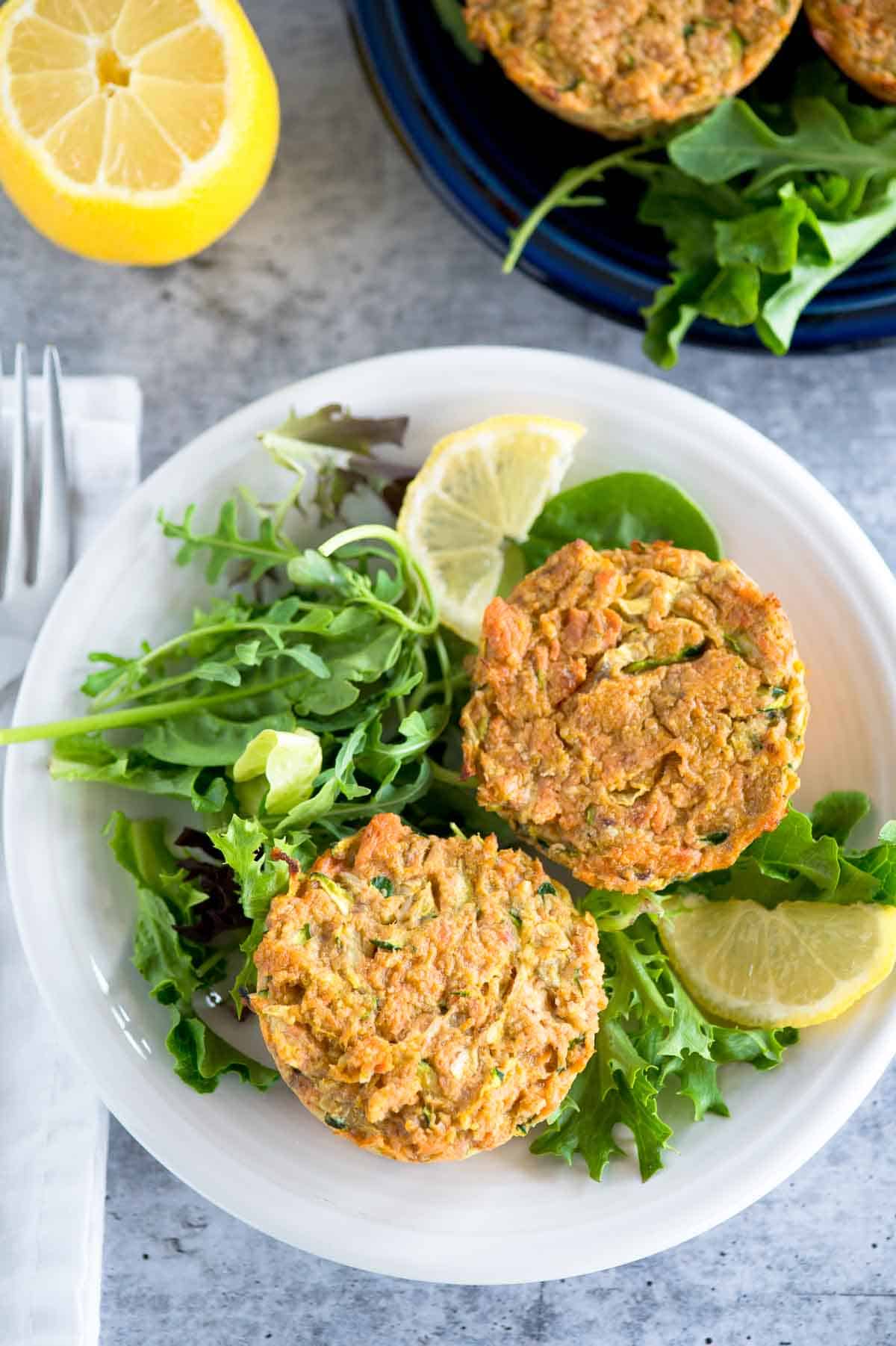 two salmon cakes on a plate with salad greens and lemon