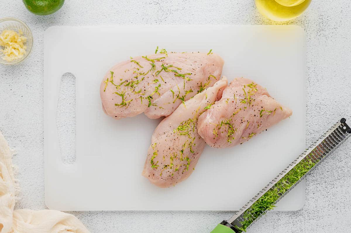raw chicken breasts seasoned with lime zest on cutting board