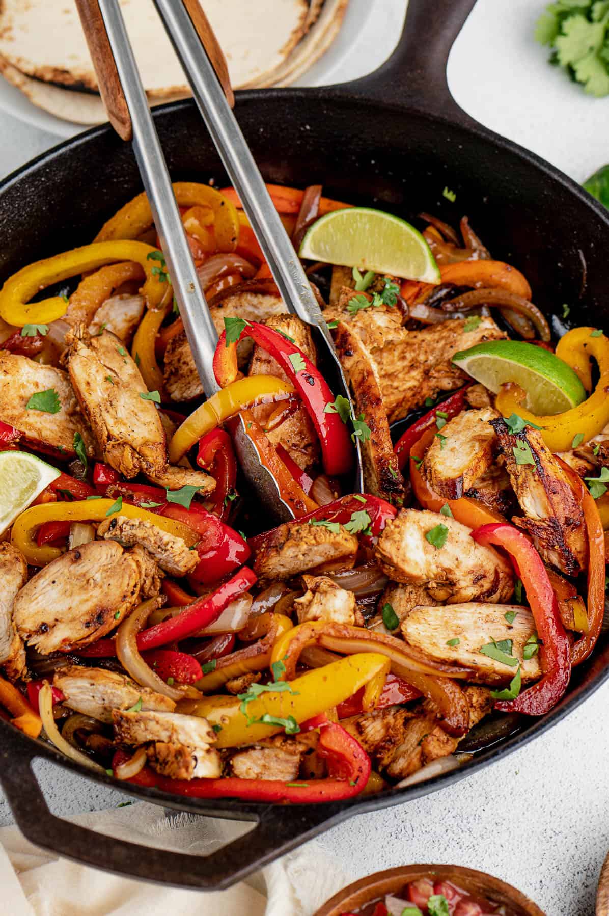 serving chicken fajitas with tongs out of cast iron skillet