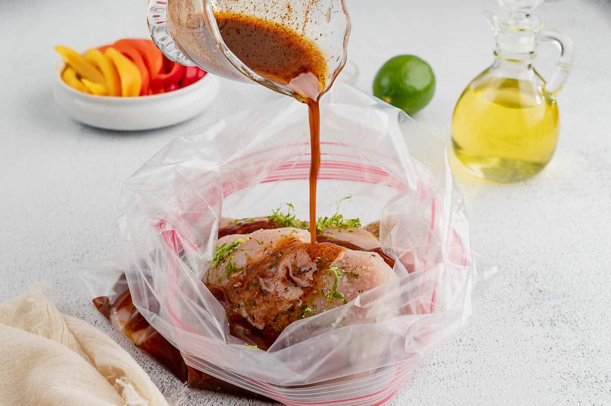 pouring marinade into ziplock bag with raw chicken