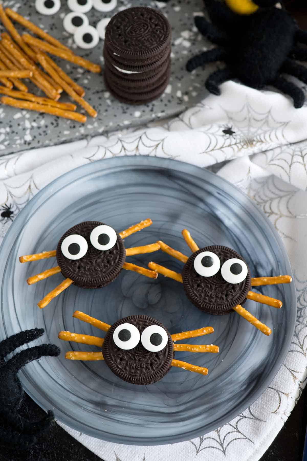 plate of oreo cookies made into spiders with pretzel sticks and candy eyeballs