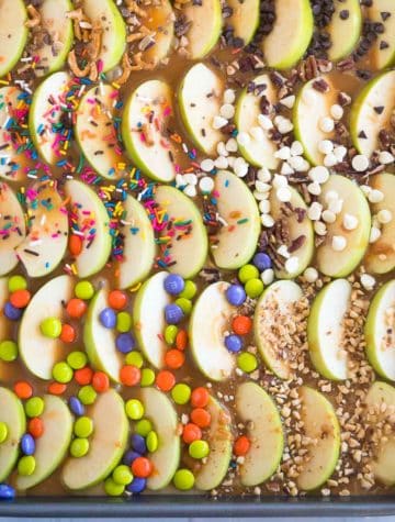sheet pan with sliced caramel apples and candy toppings