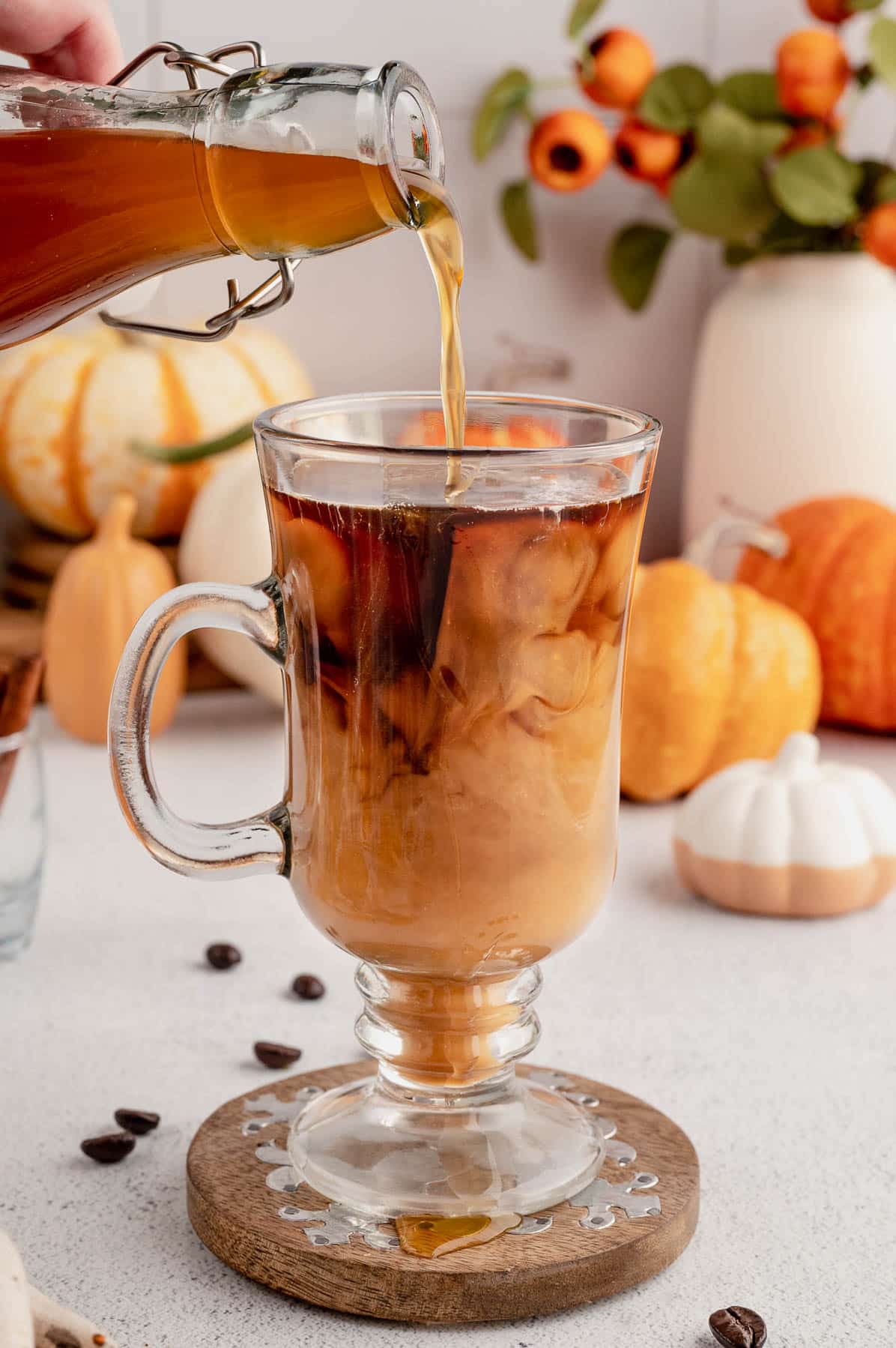 pouring pumpkin spice syrup into a glass mug of coffee for homemade pumpkin spice syrup