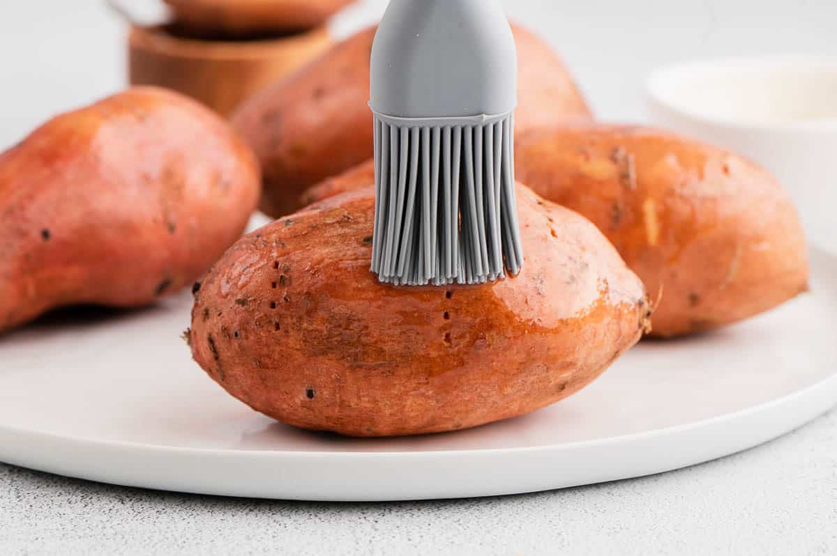 brushing olive oil on skin of sweet potato with silicone pastry brush