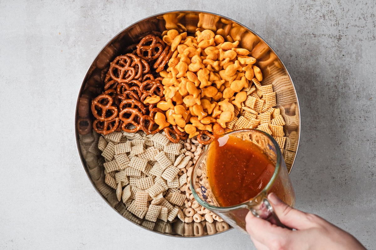 pouring butter mixture over cereal snack mixture in large bowl